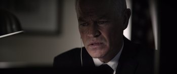 Movie still from “Monsters of Man” (2020), directed by Mark Toia – An older man wearing a suit and tie; Close Up shot, Over the shoulder angle