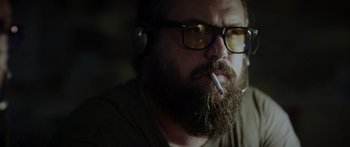 Movie still from “Monsters of Man” (2020), directed by Mark Toia – A man with a beard and glasses smoking a cigarette; Close Up shot, Low angle