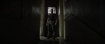 Movie still from “Monsters of Man” (2020), directed by Mark Toia – A man standing in a dark room in front of an open door; Wide shot, Low angle