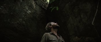 Movie still from “Monsters of Man” (2020), directed by Mark Toia – A man looking up into the sky while standing in a cave; Close Up shot, Overhead angle