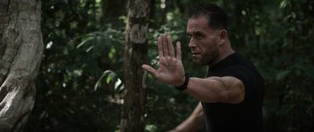 Movie still from “Monsters of Man” (2020), directed by Mark Toia – A man in a black shirt is standing in the woods; Close Up shot, Over the shoulder angle