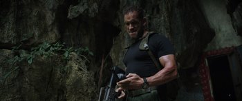 Movie still from “Monsters of Man” (2020), directed by Mark Toia – A man in black shirt holding a gun in front of a tree; Medium shot, Low angle