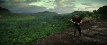 Movie still from “Monsters of Man” (2020), directed by Mark Toia – A man standing on top of a mountain near a forest; Extreme Wide shot, High angle