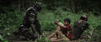 Movie still from “Monsters of Man” (2020), directed by Mark Toia – A boy sitting on the ground next to a robot in the woods; Wide shot, Low angle