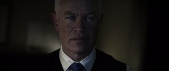 Movie still from “Monsters of Man” (2020), directed by Mark Toia – A man in a suit and a tie looking at the camera; Close Up shot, Over the shoulder angle