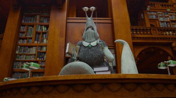 Movie still from “Monsters University” (2013), directed by Dan Scanlon – An animated character sitting in a chair in front of a book shelf; Medium shot, Low angle