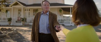 Movie still from “Monstrous” (2022), directed by Chris Sivertson – An older man wearing a brown jacket is shaking hands with an older woman wearing a brown jacket; Medium shot, Over the shoulder angle