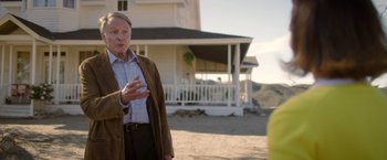 Movie still from “Monstrous” (2022), directed by Chris Sivertson – An older man standing in front of a white house; Medium shot, Over the shoulder angle