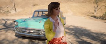 Movie still from “Monstrous” (2022), directed by Chris Sivertson – A woman in a yellow cardigan standing in front of an old car; Medium shot, Over the shoulder angle