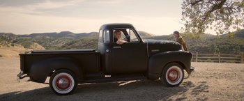 Movie still from “Monstrous” (2022), directed by Chris Sivertson – A woman sitting in the driver's seat of an old black truck; Wide shot, High angle