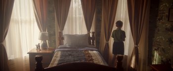 Movie still from “Monstrous” (2022), directed by Chris Sivertson – A young boy standing next to a bed in front of a window; Wide shot, High angle