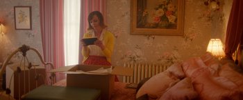 Movie still from “Monstrous” (2022), directed by Chris Sivertson – A woman standing in front of a bed looking at an ipad; Medium shot, Over the shoulder angle
