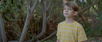 Movie still from “Monstrous” (2022), directed by Chris Sivertson – A young boy in a yellow striped t - shirt; Close Up shot, High angle