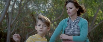 Movie still from “Monstrous” (2022), directed by Chris Sivertson – A young boy sitting next to an older woman in front of a tree; Medium shot, Over the shoulder angle
