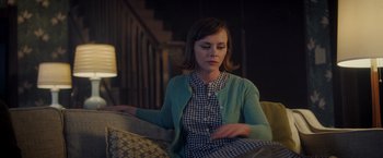 Movie still from “Monstrous” (2022), directed by Chris Sivertson – A woman sitting on top of a couch in a living room; Medium shot, Over the shoulder angle