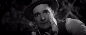 Movie still from “Monstrous” (2022), directed by Chris Sivertson – A black and white photo of a man wearing a hat; Close Up shot, High angle