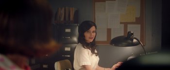 Movie still from “Monstrous” (2022), directed by Chris Sivertson – A woman sitting at a desk in an office setting; Medium shot, Over the shoulder angle