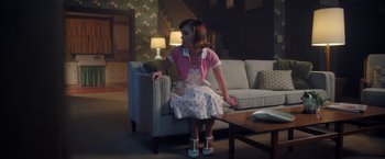 Movie still from “Monstrous” (2022), directed by Chris Sivertson – A woman sitting on top of a couch in a living room; Wide shot, High angle