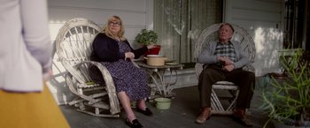 Movie still from “Monstrous” (2022), directed by Chris Sivertson – A woman sitting in a rocking chair next to a man; Wide shot, High angle