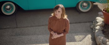 Movie still from “Monstrous” (2022), directed by Chris Sivertson – A woman in a brown dress standing on the sidewalk; Medium shot, High angle