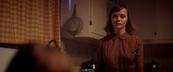 Movie still from “Monstrous” (2022), directed by Chris Sivertson – A woman standing in a kitchen looking at the camera; Medium shot, Over the shoulder angle