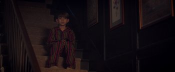 Movie still from “Monstrous” (2022), directed by Chris Sivertson – A young boy sitting on the steps of a staircase; Medium shot, High angle