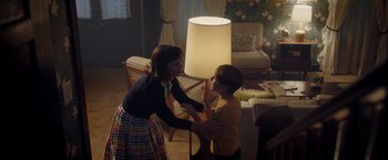 Movie still from “Monstrous” (2022), directed by Chris Sivertson – A woman and a young boy in a living room next to a lamp; Medium shot, Over the shoulder angle