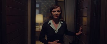 Movie still from “Monstrous” (2022), directed by Chris Sivertson – A woman standing in front of a lamp in a dark room; Medium shot, Over the shoulder angle