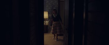 Movie still from “Monstrous” (2022), directed by Chris Sivertson – A woman is walking through a room with a lamp in the background; Wide shot, High angle