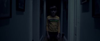 Movie still from “Monstrous” (2022), directed by Chris Sivertson – A young boy standing in a dark hallway; Medium shot, High angle