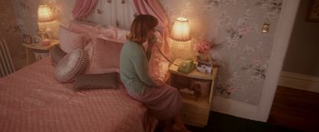 Movie still from “Monstrous” (2022), directed by Chris Sivertson – A woman sitting on a bed holding a phone to her ear; Wide shot, High angle