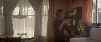 Movie still from “Monstrous” (2022), directed by Chris Sivertson – A woman standing in front of a window in a room; Medium shot, Over the shoulder angle