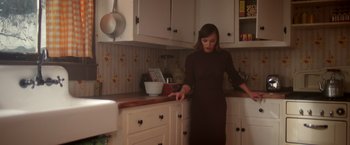 Movie still from “Monstrous” (2022), directed by Chris Sivertson – A woman in a brown dress in a kitchen; Medium shot, Low angle