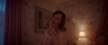 Movie still from “Monstrous” (2022), directed by Chris Sivertson – A woman smoking a cigarette while wearing a nightshirt; Medium shot, High angle