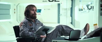Movie still from “Moon” (2009), directed by Duncan Jones – A man sitting on a chair in a room; Medium shot, Low angle