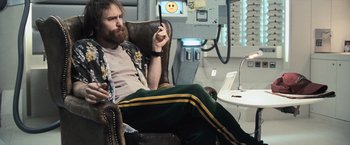 Movie still from “Moon” (2009), directed by Duncan Jones – A man sitting in a chair holding a cell phone; Medium shot, Low angle