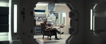 Movie still from “Moon” (2009), directed by Duncan Jones – A man sitting in a chair in a room with a lot of equipment; Wide shot, High angle