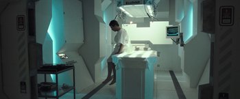 Movie still from “Moon” (2009), directed by Duncan Jones – A man sitting on top of a table in a room; Wide shot, High angle