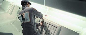 Movie still from “Moon” (2009), directed by Duncan Jones – A man in a gray uniform is using a computer keyboard; Medium shot, Overhead angle