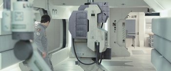 Movie still from “Moon” (2009), directed by Duncan Jones – An image of a machine in a room with white walls; Wide shot, Overhead angle