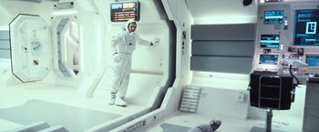 Movie still from “Moon” (2009), directed by Duncan Jones – A man in a spacesuit standing in a room; Wide shot, Overhead angle