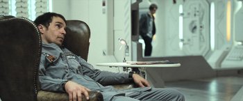 Movie still from “Moon” (2009), directed by Duncan Jones – A man sitting in a chair next to a table; Medium shot, Over the shoulder angle