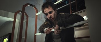 Movie still from “Moon” (2009), directed by Duncan Jones – A man leaning on a railing holding a knife; Medium shot, Low angle