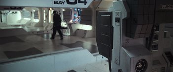 Movie still from “Moon” (2009), directed by Duncan Jones – A man walking in a room with a large display of electronics; Wide shot, High angle