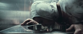Movie still from “Moon” (2009), directed by Duncan Jones – A person bending over a pan in a kitchen; Close Up shot, High angle