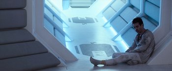 Movie still from “Moon” (2009), directed by Duncan Jones – A person sitting on the ground in a room; Wide shot, Overhead angle