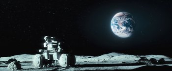 Movie still from “Moon” (2009), directed by Duncan Jones – An astronaut on the surface of the moon with the earth in the background; Extreme Wide shot, High angle