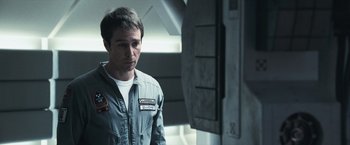 Movie still from “Moon” (2009), directed by Duncan Jones – A man in a gray suit standing in a room; Close Up shot, Over the shoulder angle
