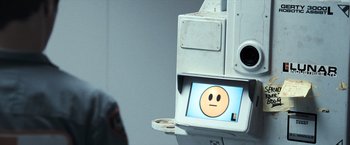 Movie still from “Moon” (2009), directed by Duncan Jones – An image of an electronic device with a sad face on it; Close Up shot, Over the shoulder angle