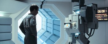 Movie still from “Moon” (2009), directed by Duncan Jones – A man standing next to an open door looking at a camera; Medium shot, Overhead angle
